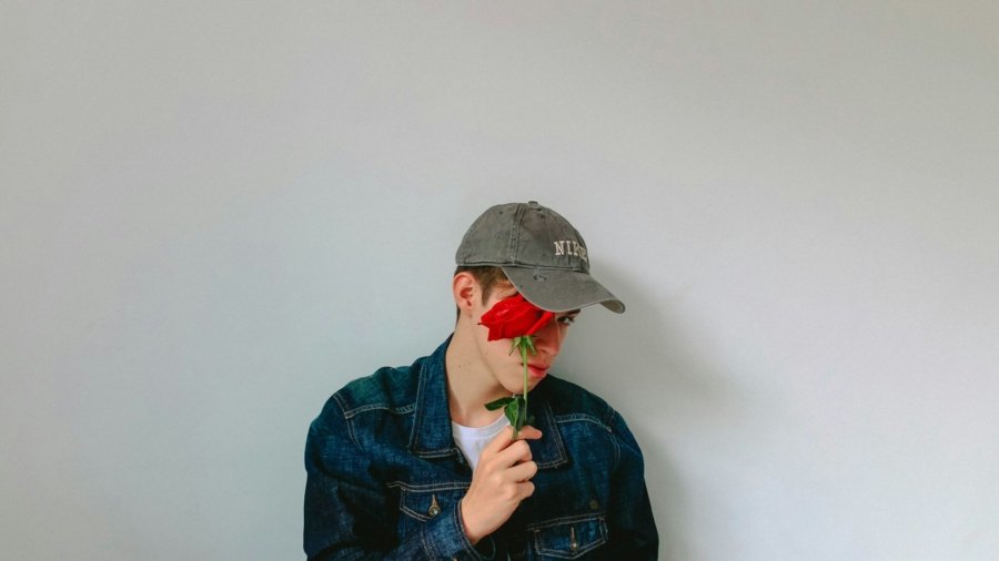 man in denim jacket holding rose on his face